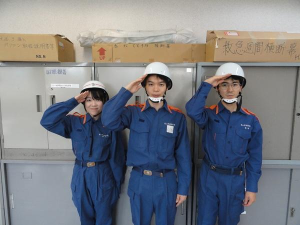 宮野 真名美さん、高橋 翔太朗さん、河合 秀樹さんが、消防のユニフォームを着て、ヘルメットをかぶり敬礼のポーズをしている写真